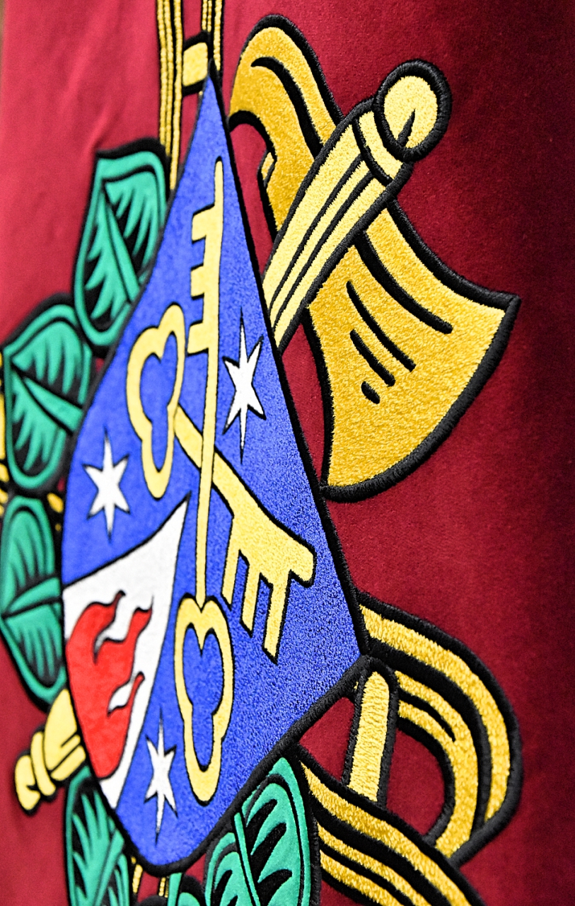 Detail výšivky heraldického znaku obce Šimanov s hasičskými motivy.